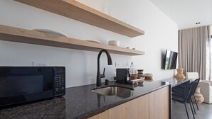 A modern kitchen with a built-in microwave, a sink, and wooden shelves above. - Adults Only! Desecheo Suite II at Ocaso Luxury Villas (Rincon)