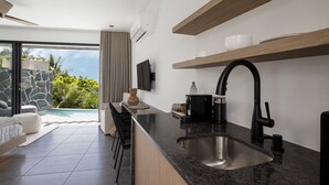Una cocina moderna con un lavamanos grande, estantes empotrados y vistas a una piscina y follaje.