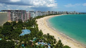 A coastal cityscape with a wide sandy beach, a clear blue sea, and high-rise buildings in the background.