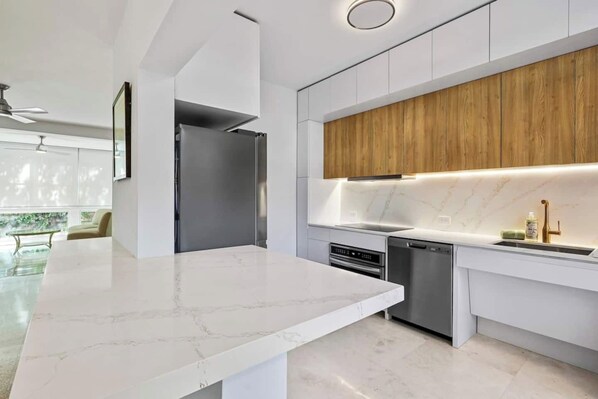 A modern kitchen with white marble countertops, stainless steel appliances, and wooden cabinetry.