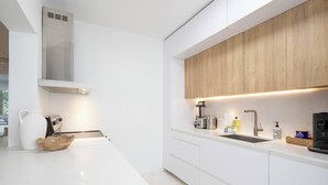 A modern kitchen with white cabinetry, a wooden upper cabinet, a stainless steel range hood, and a countertop with various appliances and items. - Villa Georgetti Hidden Gem in Miramar, SJ | Power Generator, Water Cistern, Parking (San Juan)