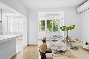 Uma sala de jantar moderna com mesa de vidro, paredes brancas e vista para o verde lá fora.