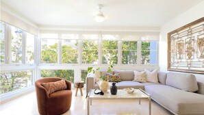 A spacious living room with large windows, a sofa, a coffee table, and a decorative metal piece on the wall.