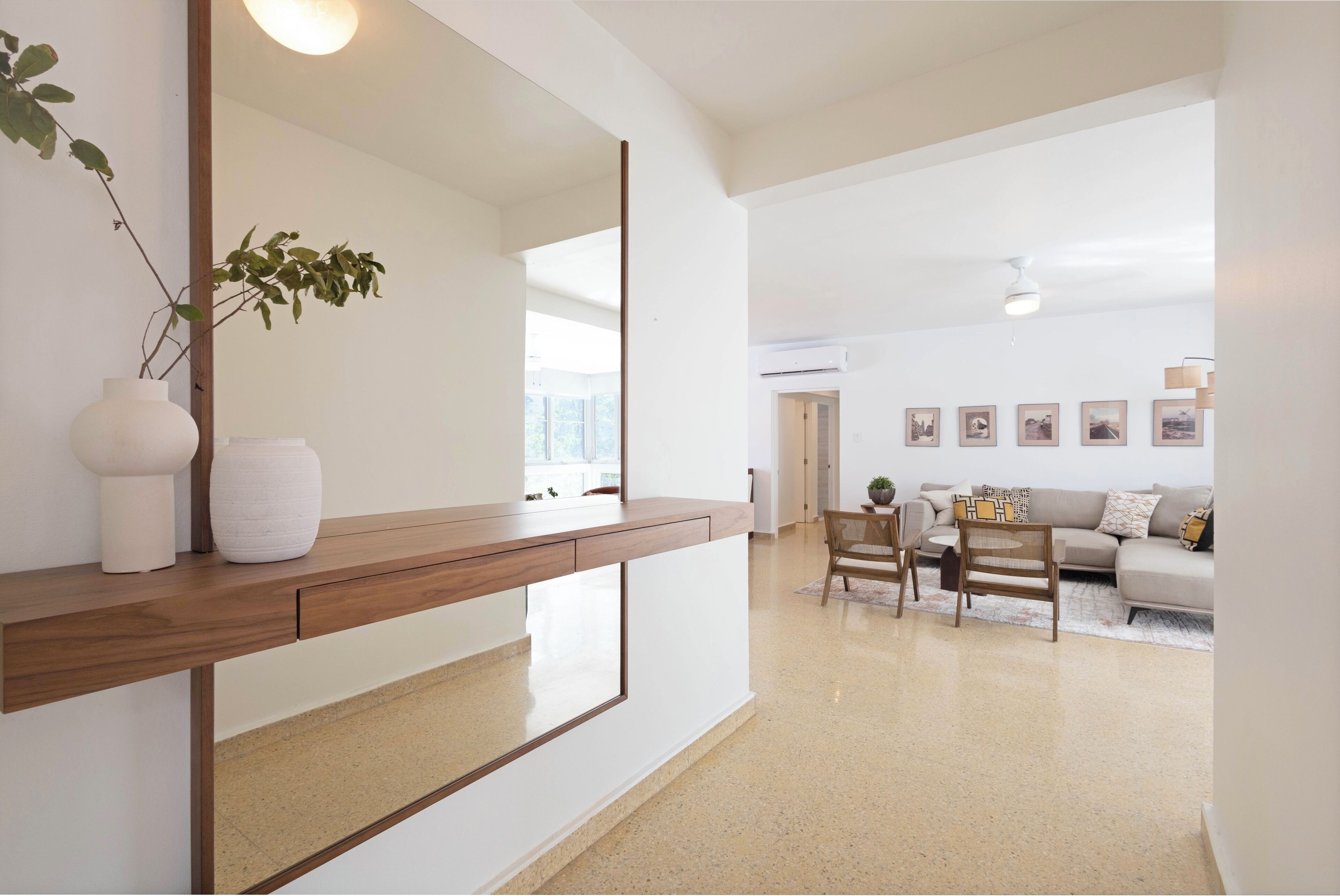A modern living room with a wooden console table, a large mirror, a sofa, and a dining area.