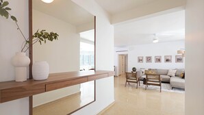A modern living room with a wooden console table, a large mirror, a sofa, and a dining area.