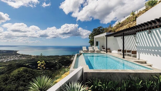 Un área de piscina moderna con vista al mar y una colina.