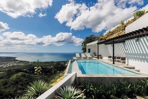 A modern pool area with a view of the sea and a hillside.