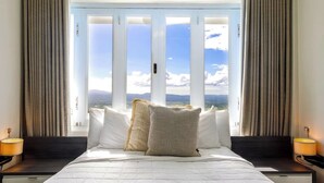 Habitación de hotel con una cama grande, ropa de cama blanca y vistas a las montañas a través de ventanales de piso a techo.