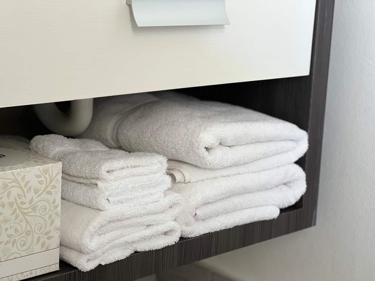Toallas blancas apiladas ordenadamente sobre una repisa en un baño.