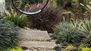 A garden with a hanging swing, stone pathway, and various plants.
