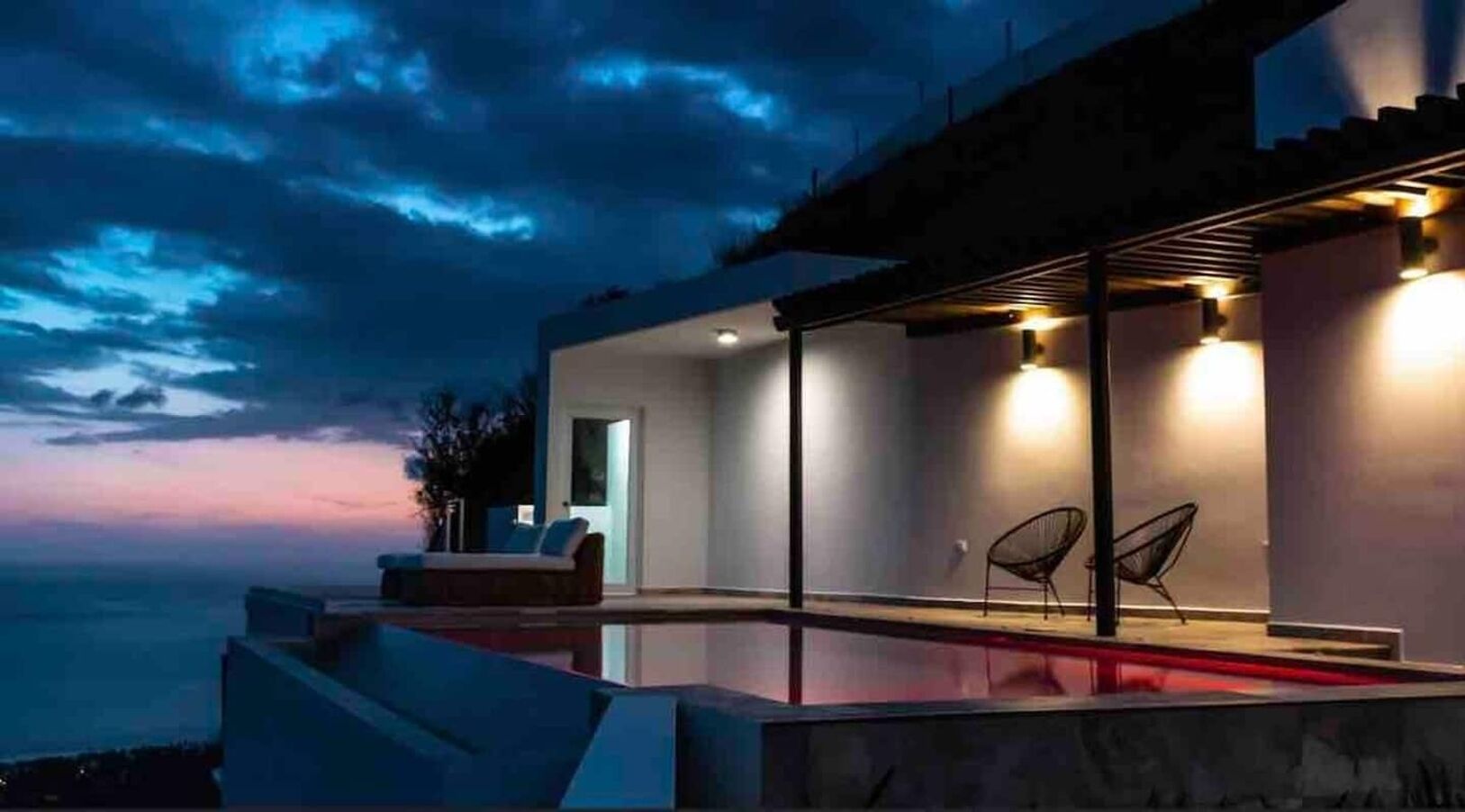Un área de piscina moderna al aire libre con vista al océano al anochecer.