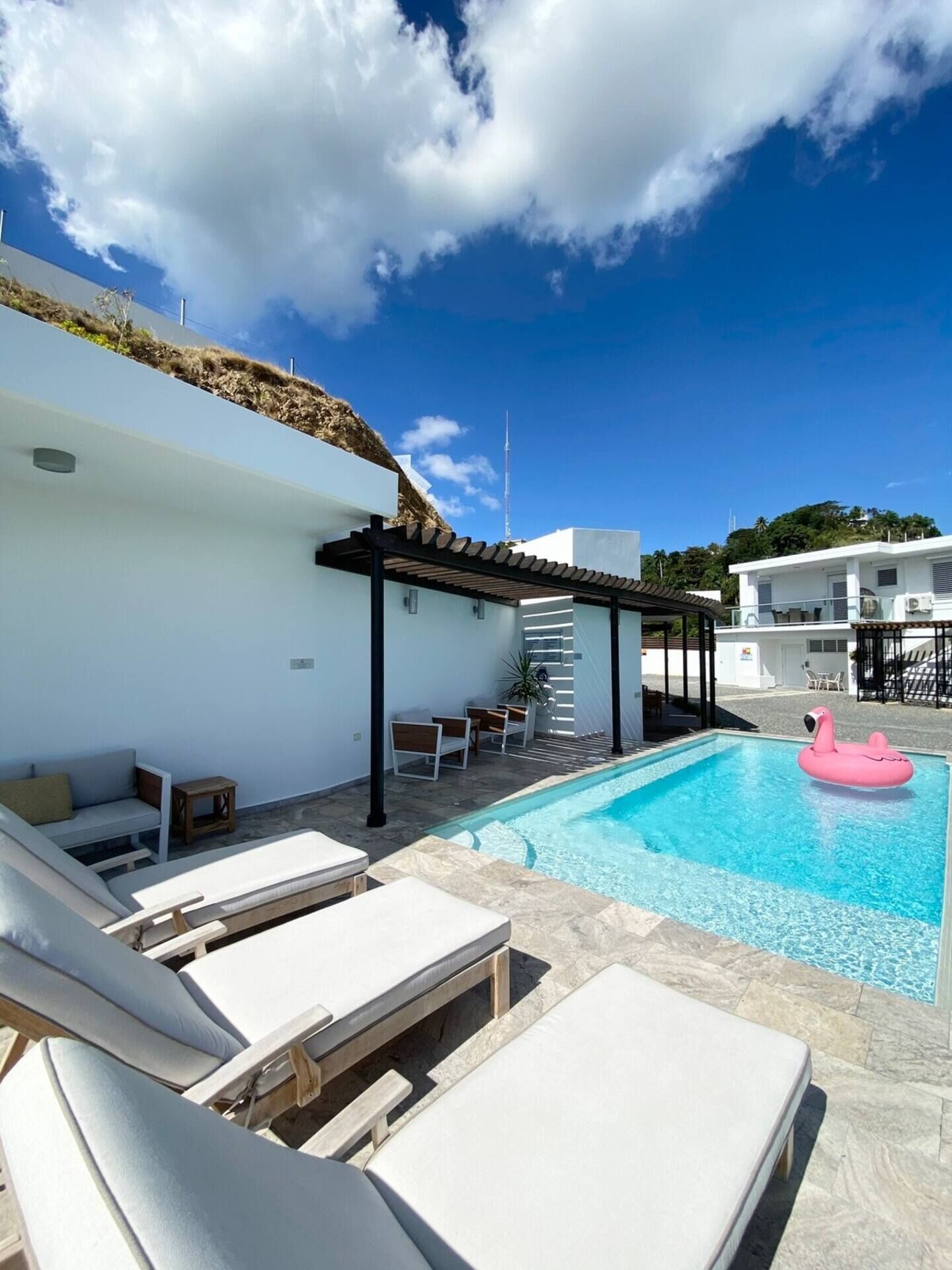 A modern outdoor pool area with lounge chairs, a pergola, and a pink flamingo float.