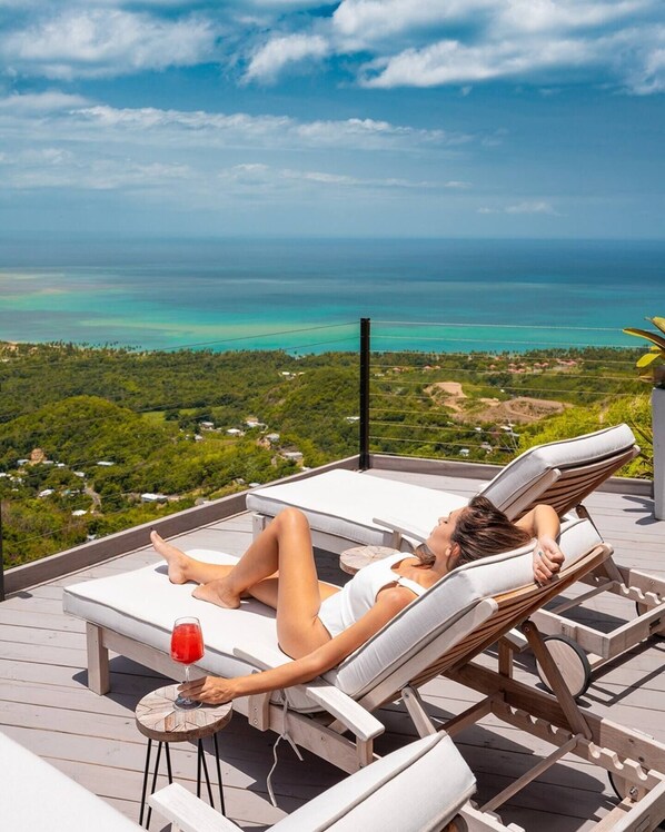 Una persona descansando en una tumbona con vistas al océano y un paisaje tropical.