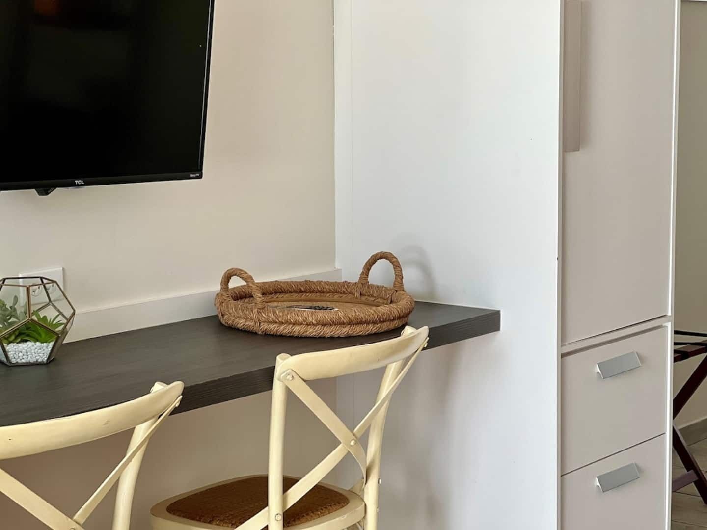 A modern room with a dark wood desk, a woven basket, a small potted plant, and a white chair.