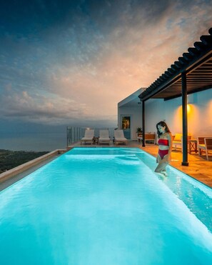 Una piscina con vista sull'oceano, sedie a sdraio e un'area relax all'ombra.