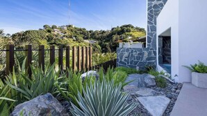 Una casa moderna con fachada de piedra, cerca de madera y vistas a una colina con edificios.