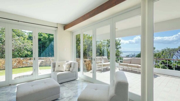 Ein geräumiges Wohnzimmer mit großen Schiebeglasüren, die auf eine Terrasse mit Meerblick führen.