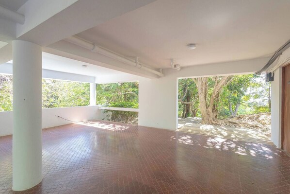 A spacious room with a tiled floor, large windows, and a view of a tree-lined outdoor area. - Stunning 1950's grand house nestled in lush greenery overlooking the bay (Aguadilla)