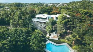 Ein modernes Haus, umgeben von dichtem Wald, mit Swimmingpool und einer kleinen Laube.