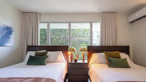 Ein Hotelzimmer mit zwei Betten, einem Nachttisch mit Lampen und einem Fenster mit Vorhängen.
