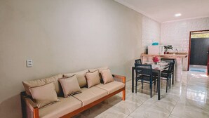 A living room with a sofa, dining table, chairs, and a kitchen area with a refrigerator and sink. - Casa Refúgio (Cruz)