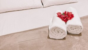 A neatly made bed with white linens and two rolled towels with red flowers on a beige carpet. - Casa Refúgio (Cruz)