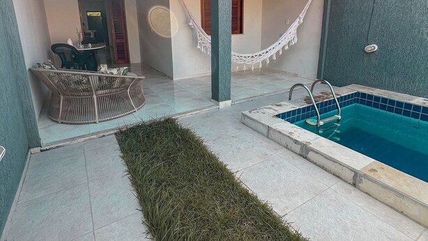 A pool area with a tiled deck, a hammock, and a seating area with chairs. - Casa Refúgio (Cruz)