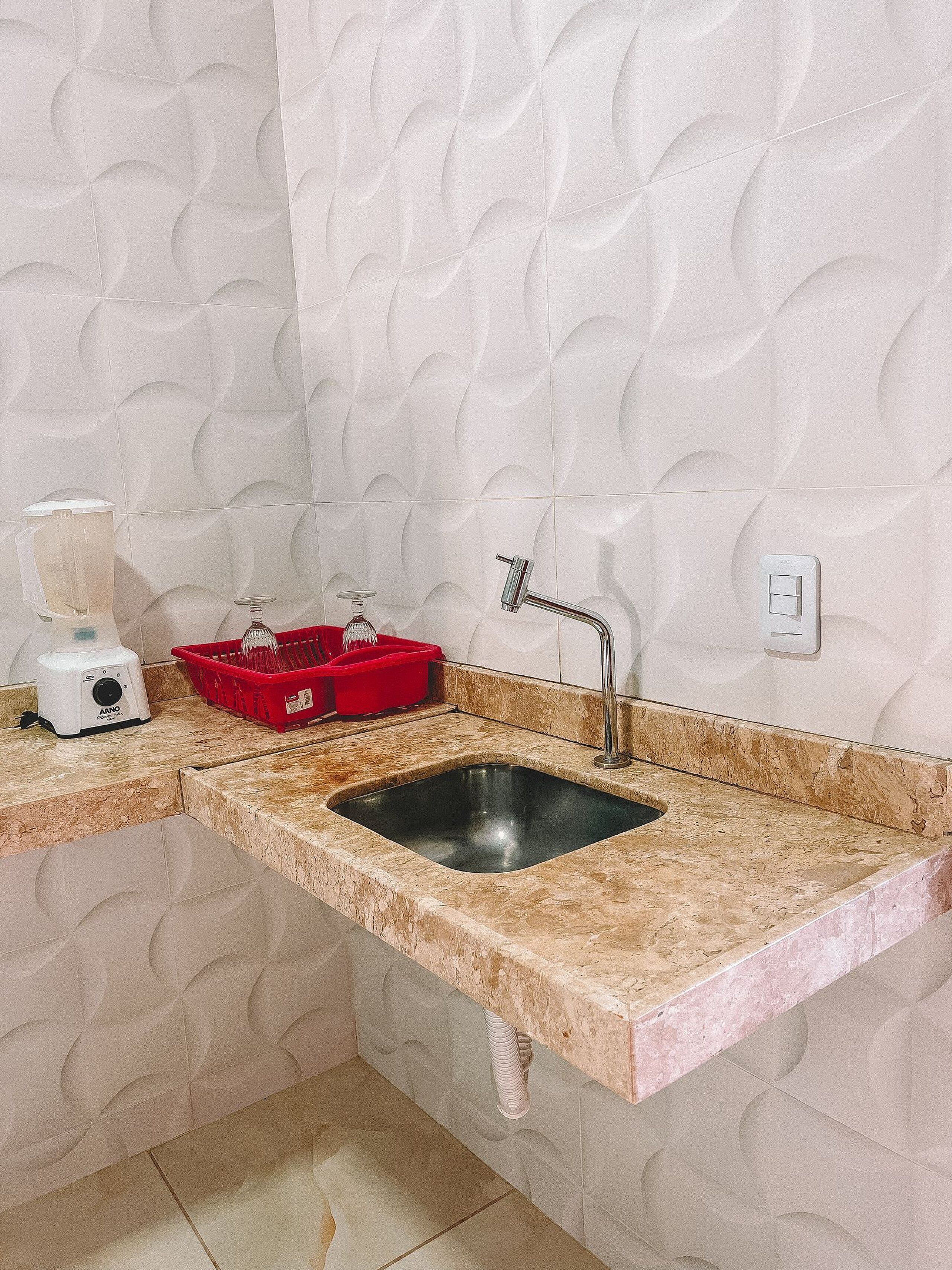 A kitchen with a granite countertop, a sink, a red dish rack, and a blender.
