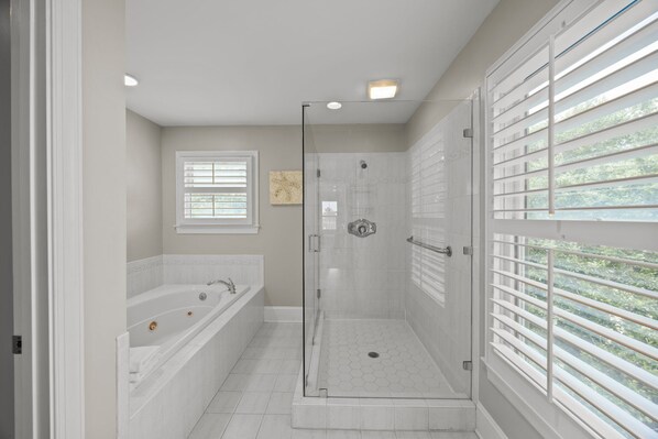 Un baño moderno con ducha acristalada, bañera independiente y ventana con persianas.