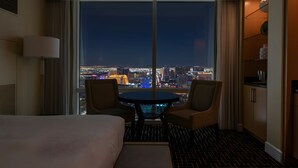Ein Hotelzimmer mit großem Fenster und Blick auf die nächtliche Stadt.