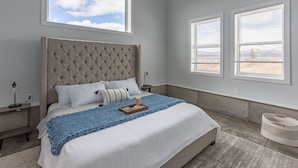 Un dormitorio con una cama grande, dos mesitas de noche, una ventana con persianas y vistas al exterior.