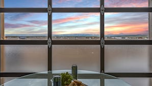 Una mesa con un plato de comida y una lata, vista a través de una ventana con vista al atardecer.