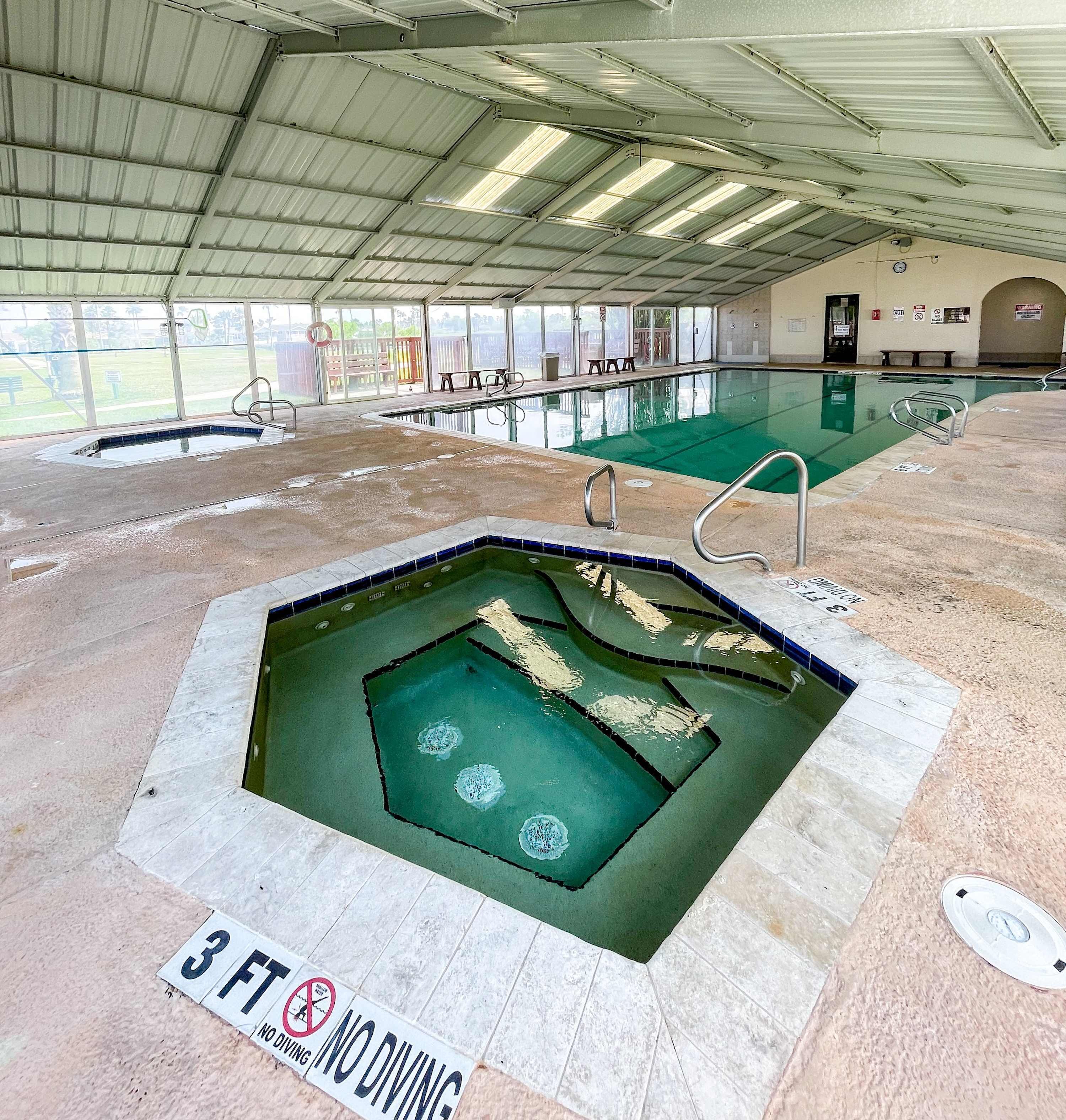 An indoor swimming pool with a 3 ft no diving sign, tiled floor, and a covered roof.