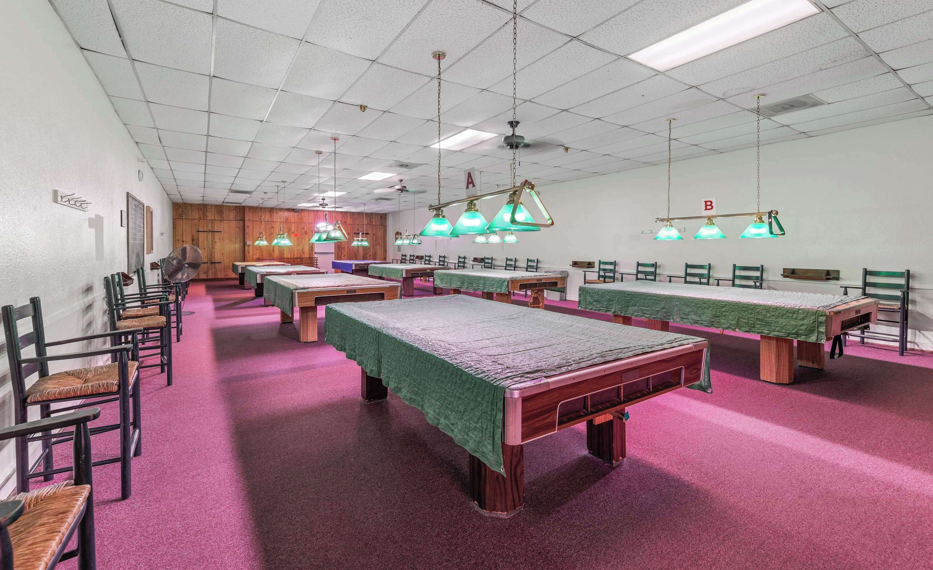 A room with multiple beds, chairs, and tables, with green lamps and a ceiling fan.