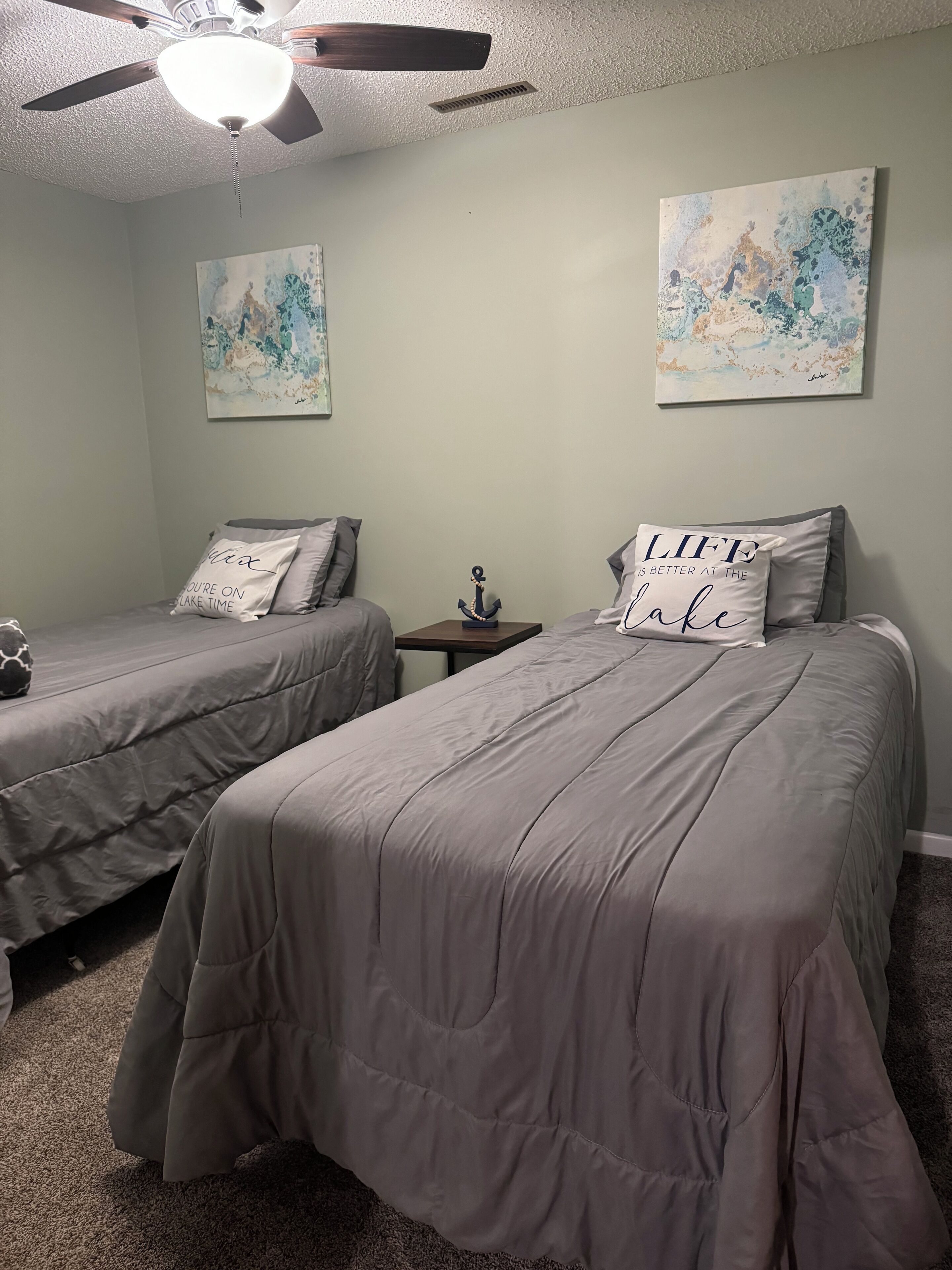 A bedroom with two beds, a ceiling fan, and artwork on the walls.