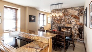 A kitchen with a stone accent wall, a large island with a sink, and a dining area with chairs and a table.