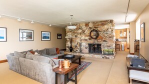 A living room with a stone fireplace, a sofa, a coffee table, and a laptop on a desk.
