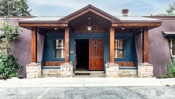 A two-story building with a wooden front door, a porch with stone steps, and a metal roof.