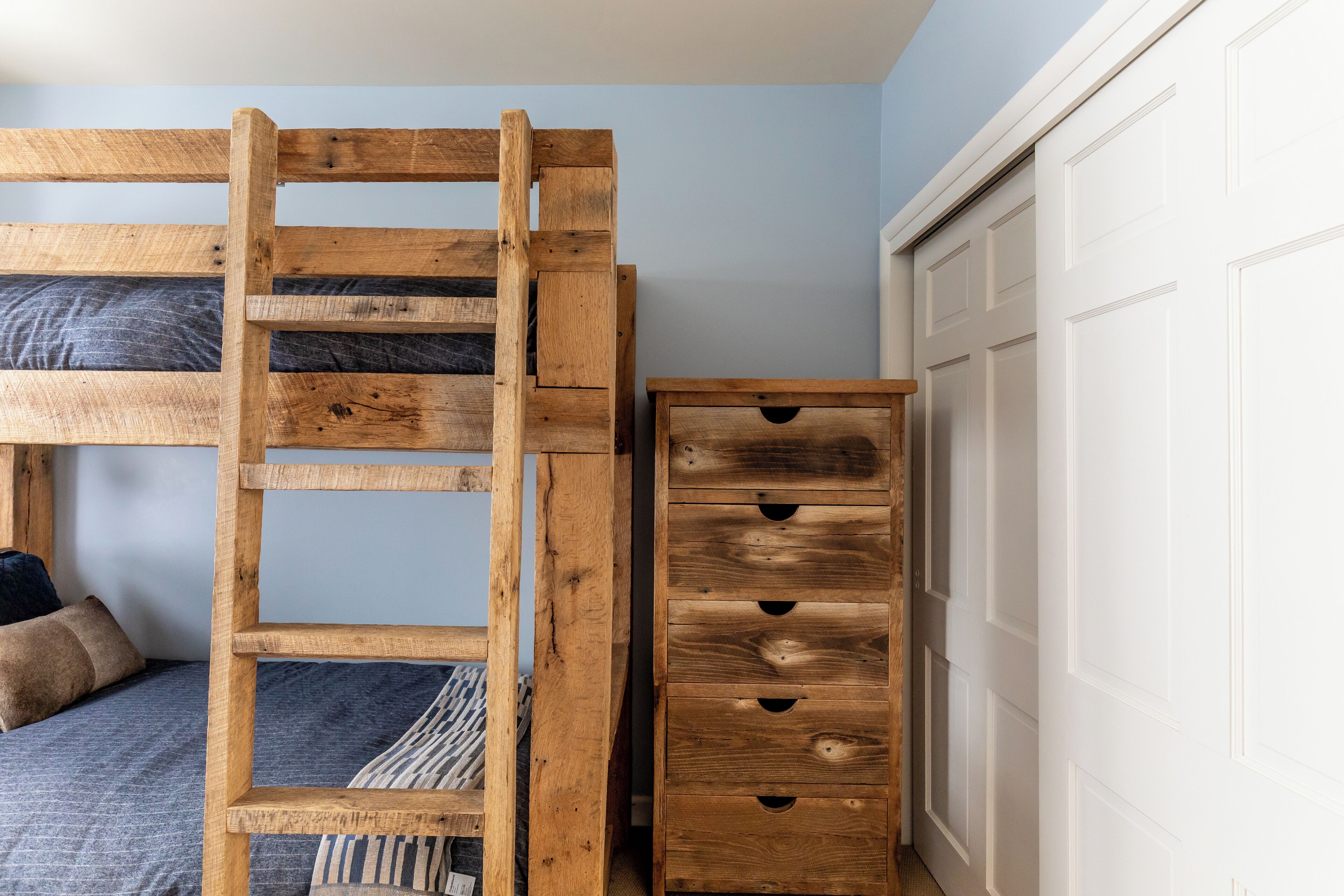 A bunk bed with a wooden ladder, a dresser with drawers, and a white door in a room with light blue walls.