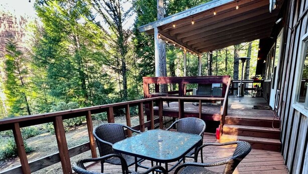 A wooden deck with wicker chairs and a table, surrounded by trees. - Pioneer Cabin Retreat (Gasquet)