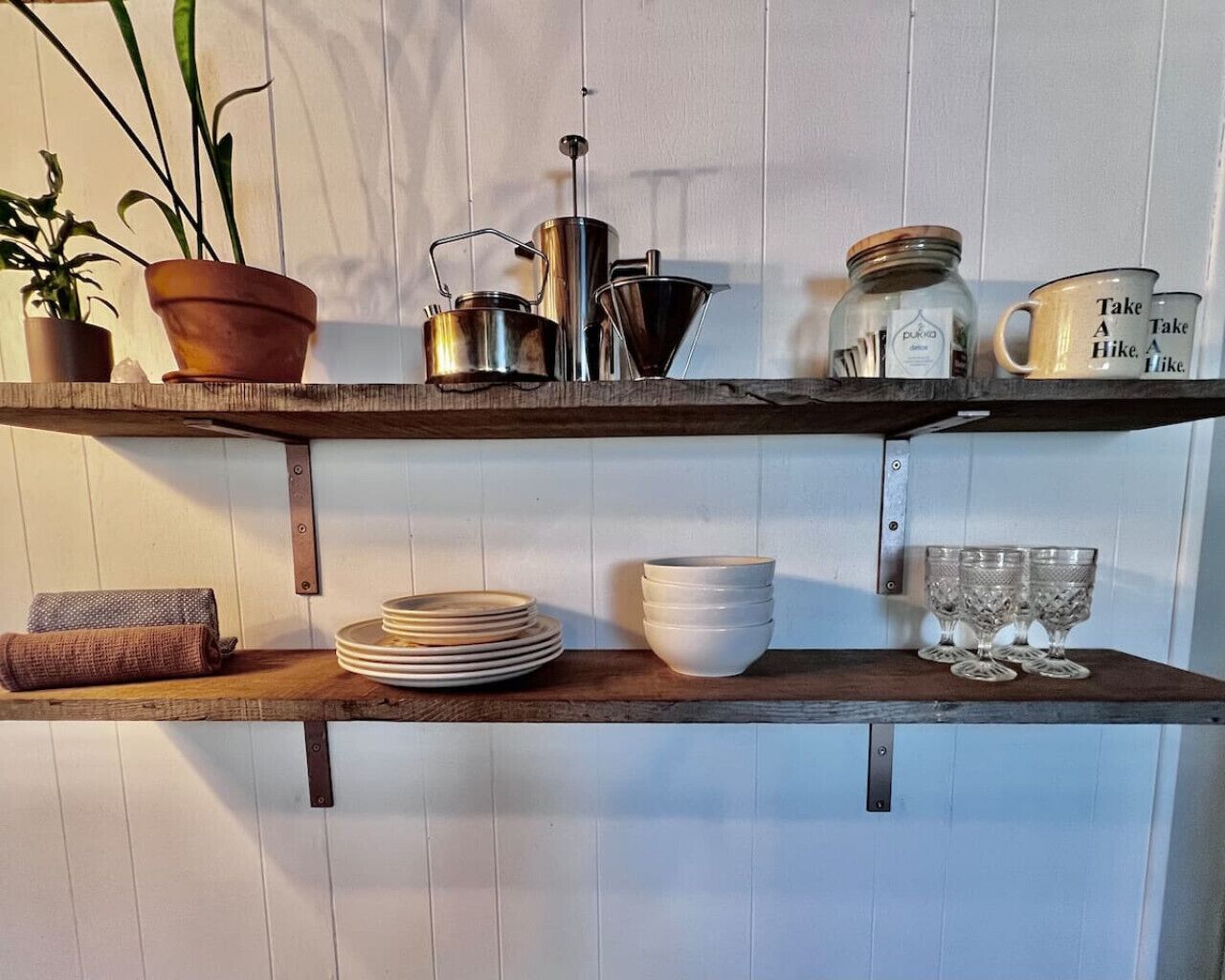 A wooden shelf with kitchen utensils, plates, and glasses.