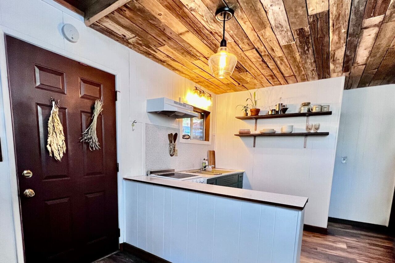 A kitchen with a wooden ceiling, a dark brown door, and a white countertop.