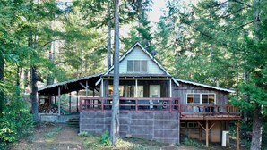 A rustic cabin with a porch, surrounded by dense forest. - Pioneer Cabin Retreat (Gasquet)