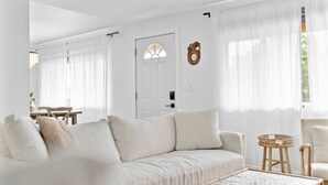 Una sala de estar moderna con un sofá blanco, una mesa de centro de madera y cortinas traslúcidas.