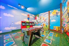 A room with a foosball table, arcade games, and colorful murals. - The Luxurious Bear's Den Estate-TB009 (Kissimmee)