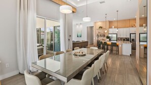 Een moderne keuken met een centraal eiland, hanglampen en een eethoek met een glazen tafel.