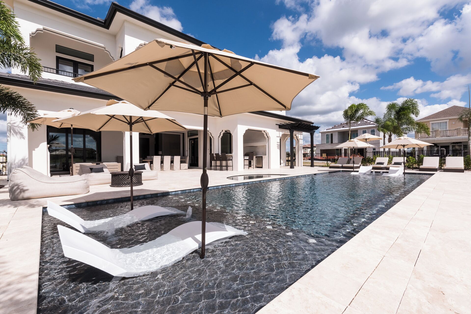 Una piscina con sillas de descanso y sombrillas, rodeada por una casa moderna con un patio.