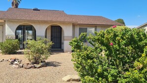 A single-story house with a garage, a front door, and a small garden with rocks and shrubs. - Calm saguaro cacti house with palms and oleanders, chirping quails.  (Phoenix)