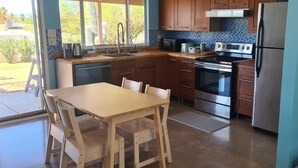 A modern kitchen with wooden cabinets, stainless steel appliances, a dining table with chairs, and a view of the outdoors. - Calm saguaro cacti house with palms and oleanders, chirping quails.  (Phoenix)