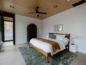A bedroom with a wooden bed, a green rug, a ceiling fan, and a view through an open door.